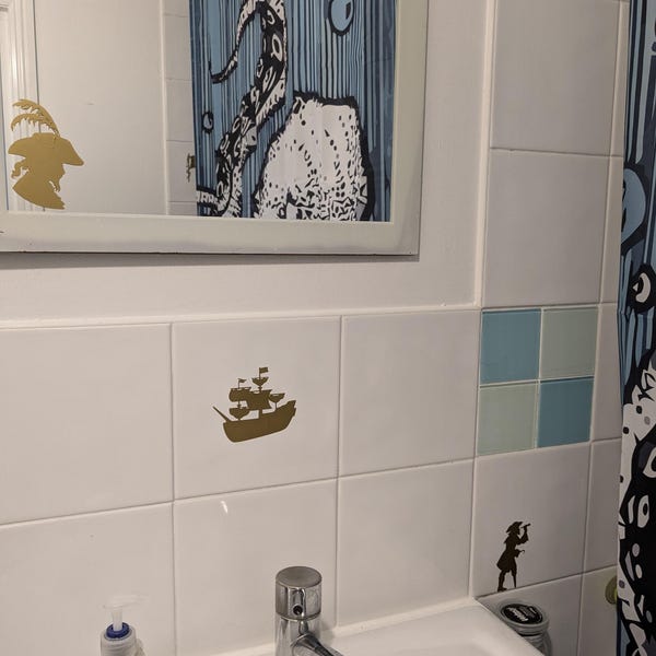 Small gold pirate-themed decals applied to white bathroom tiles.