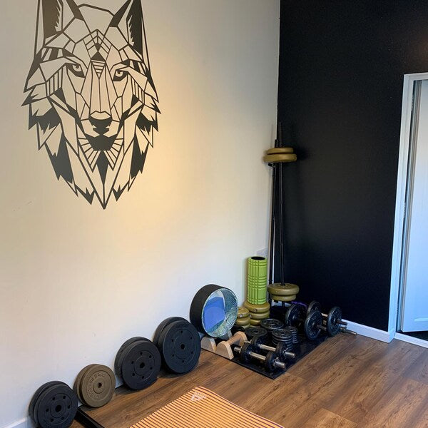 Black geometric wolf head decal above exercise equipment in a home gym.