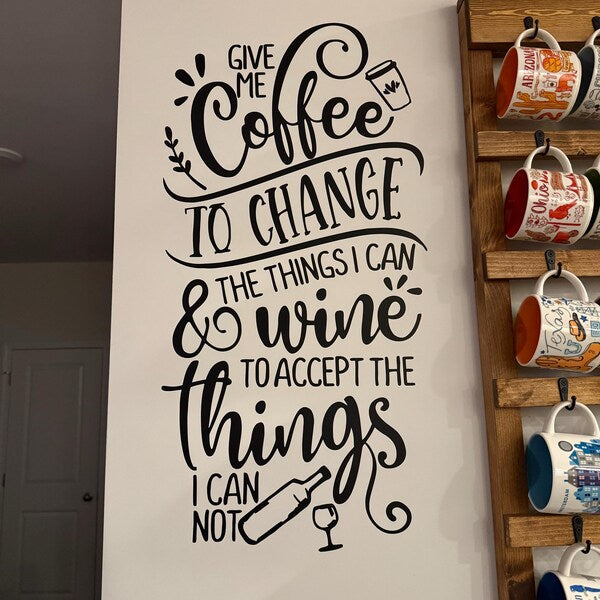 Black coffee and wine quote lettering on a pale kitchen wall beside a mug rack.