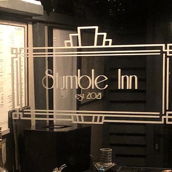 Light-coloured custom inn lettering with a geometric border on glass.