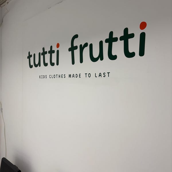 Green and red tutti frutti shop logo on a white wall.