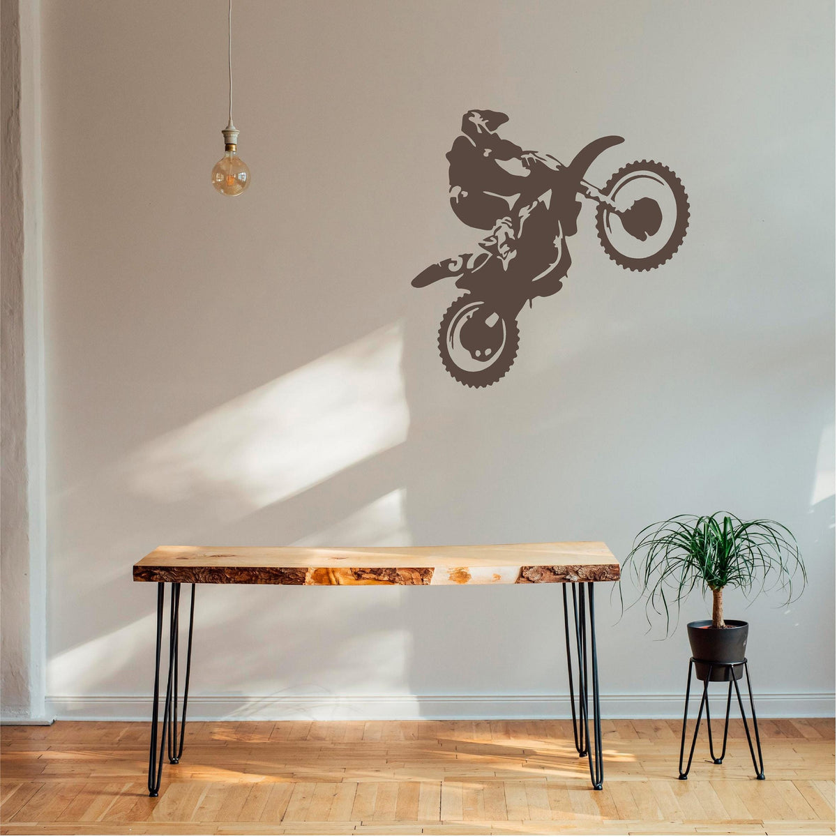 Brown motorbike wheelie rider wall decal above a wooden console bench beside a hanging bulb and plant.