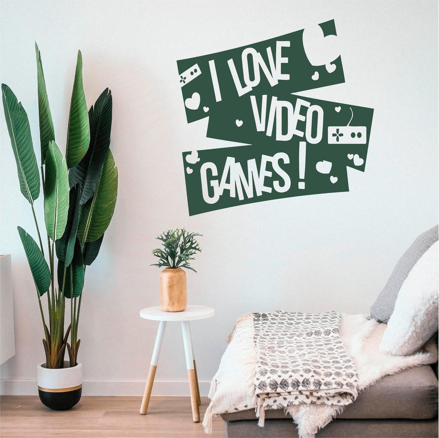 Dark green I Love Video Games wall decal with controllers and hearts beside a large plant and cushioned bench.