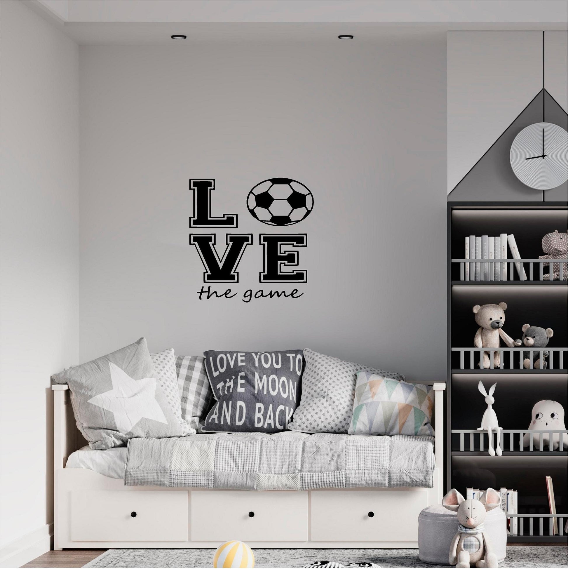 Black Love the Game football wall decal above a grey daybed beside toy shelves.