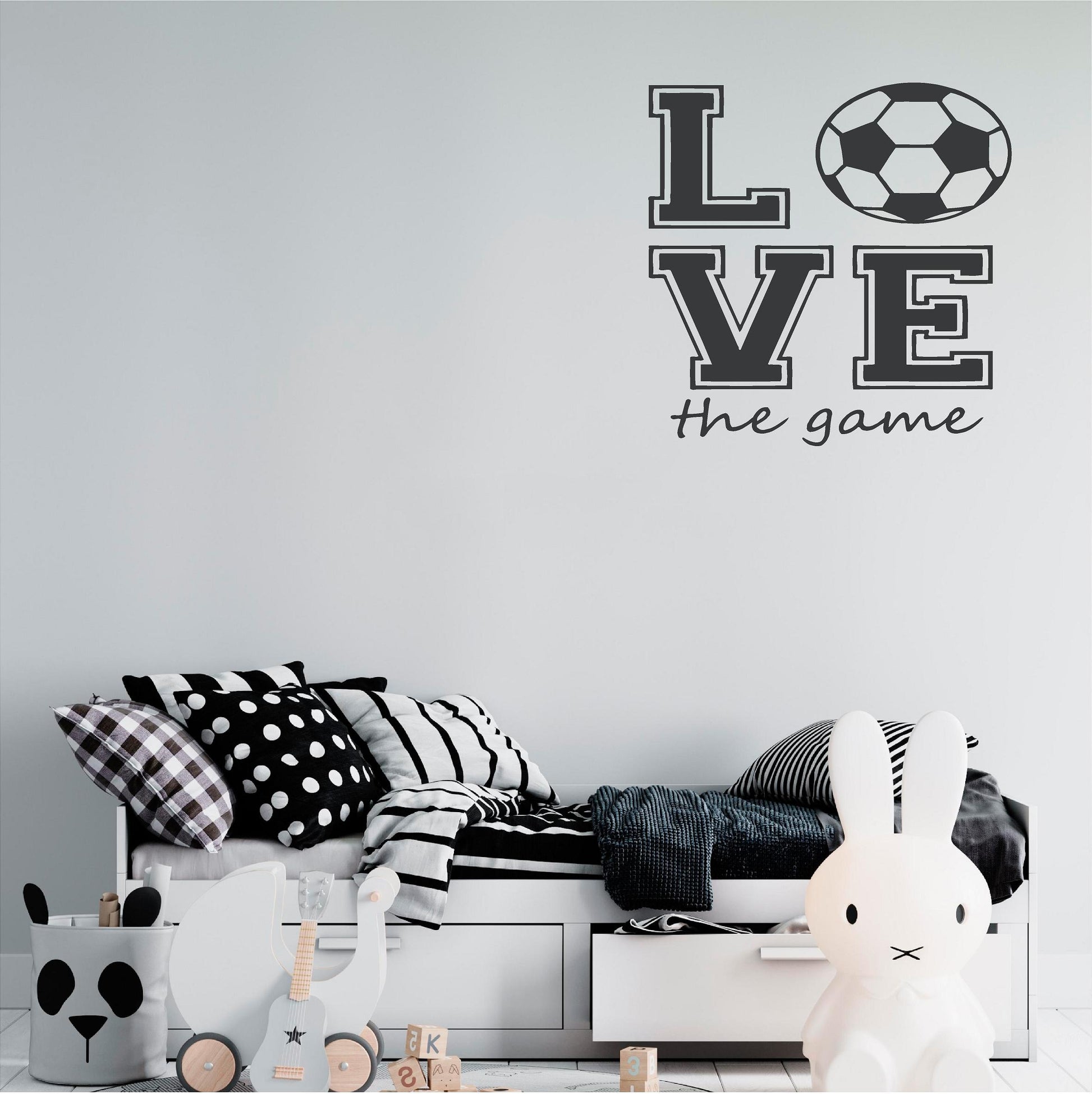 Dark grey Love the Game football wall decal above a child's bed with black and white cushions.