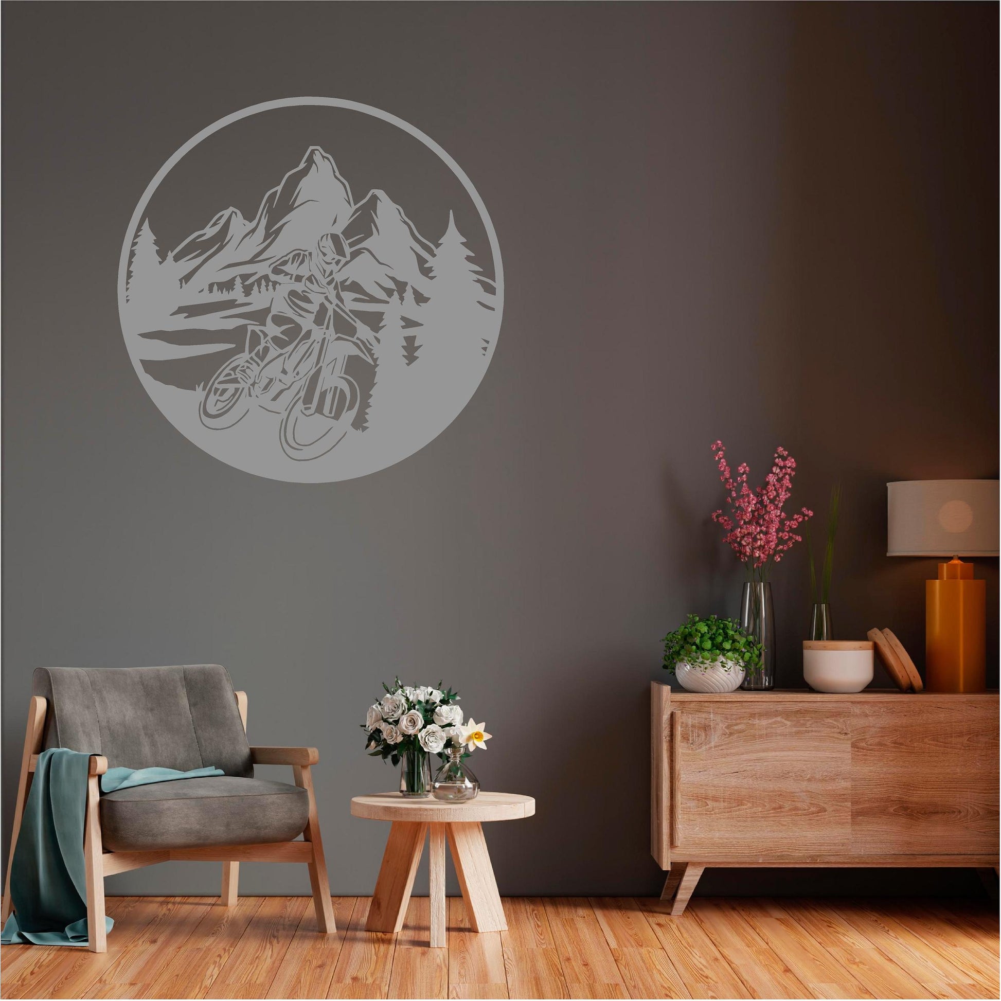Grey circular mountain biker wall decal with mountains and pine trees above an armchair on a dark wall.