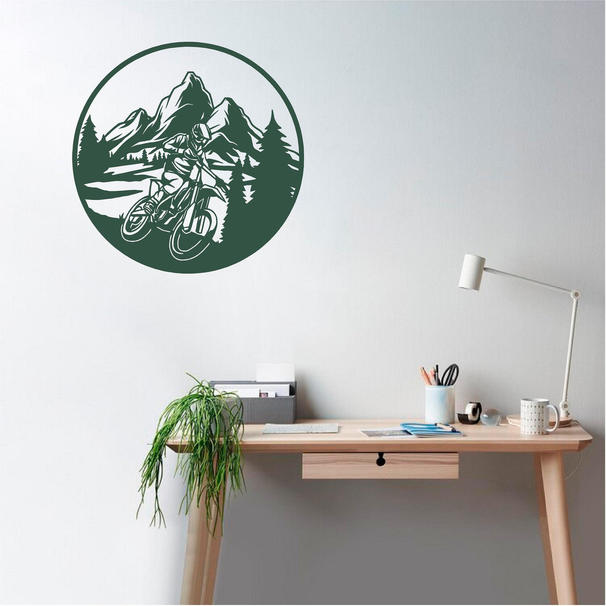 Dark green circular mountain biker wall decal with mountains and pine trees above a study desk.