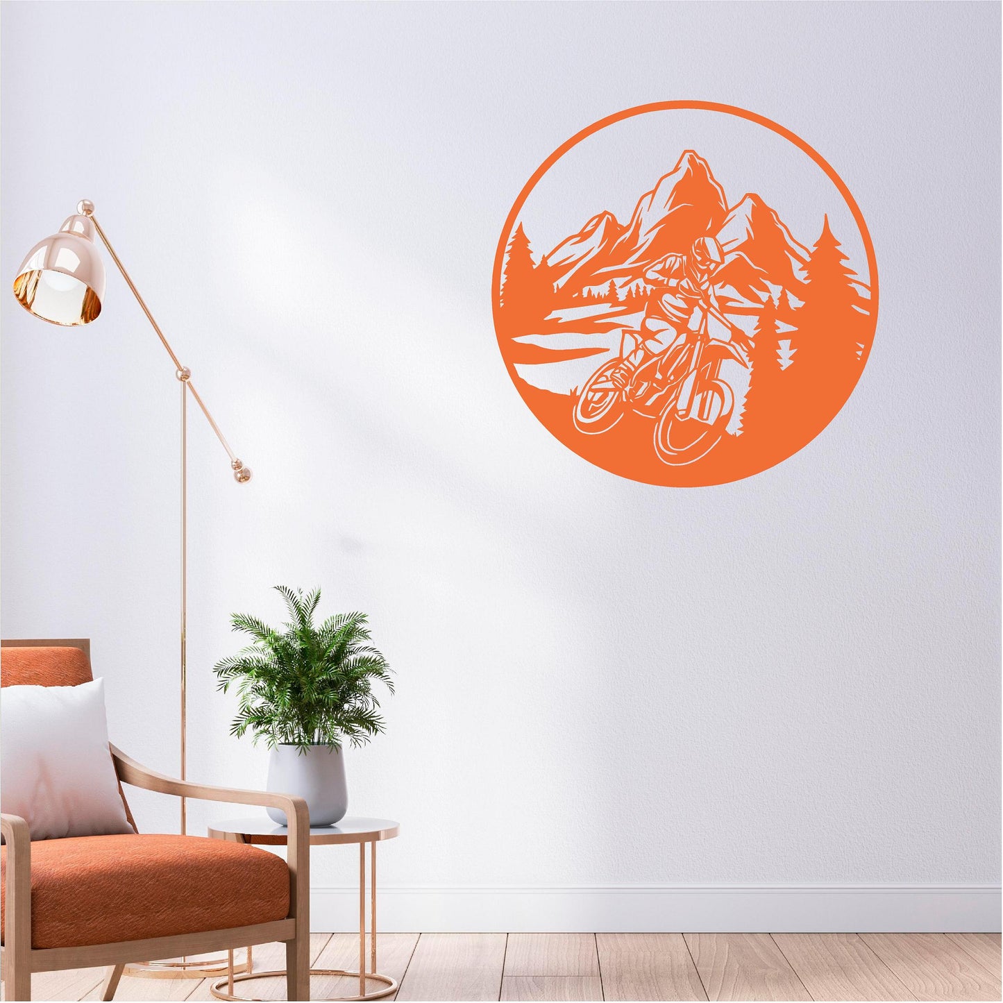 Orange circular mountain biker wall decal with mountains and pine trees above a fern beside an orange chair.