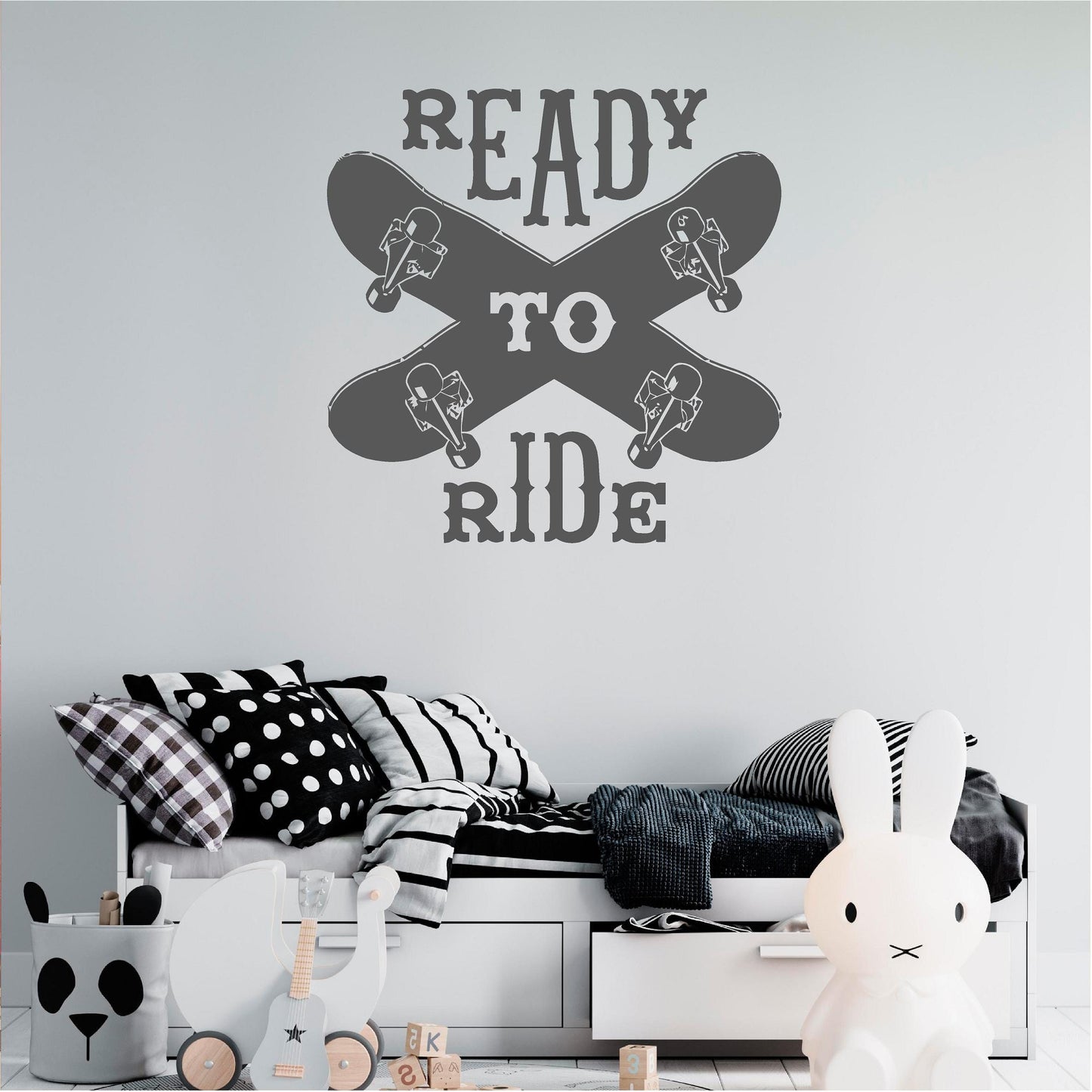 Dark grey Ready to Ride wall decal with two crossed skateboards above a child's daybed.