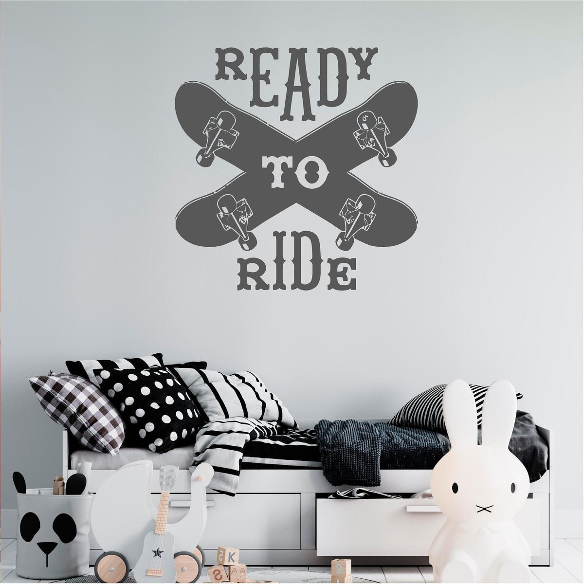 Dark grey Ready to Ride wall decal with two crossed skateboards above a child's daybed.