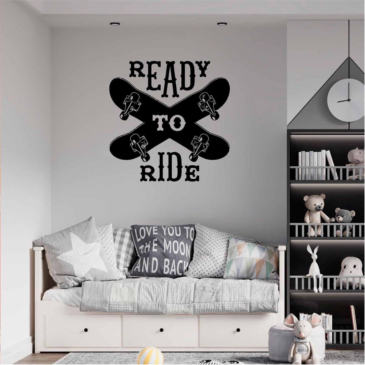 Black Ready to Ride wall decal with two crossed skateboards above a grey daybed beside shelves.