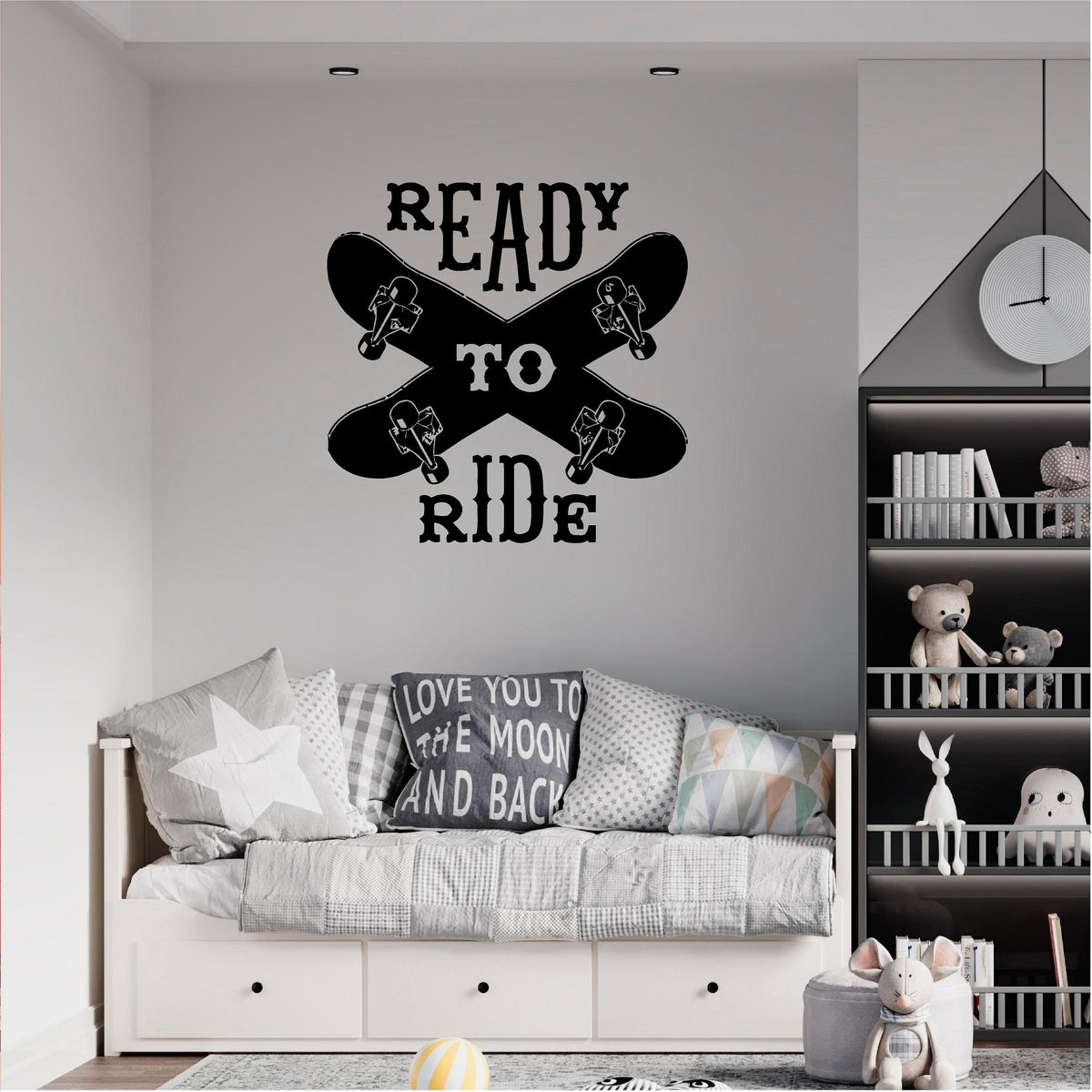Black Ready to Ride wall decal with two crossed skateboards above a grey daybed beside shelves.