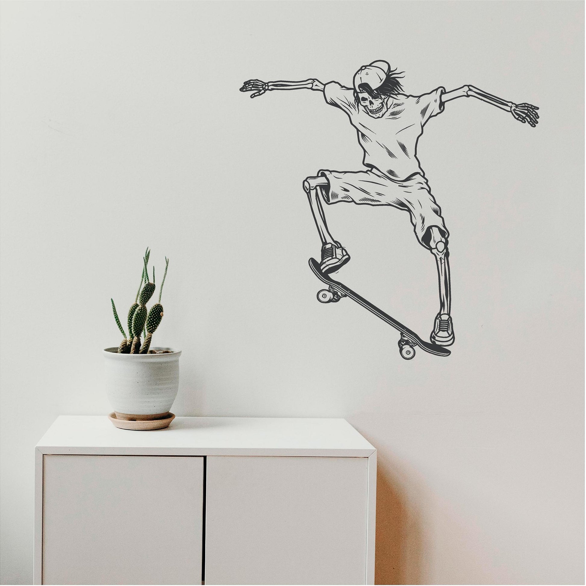 Dark grey skeleton skateboarder wall decal above a white cabinet beside a cactus.