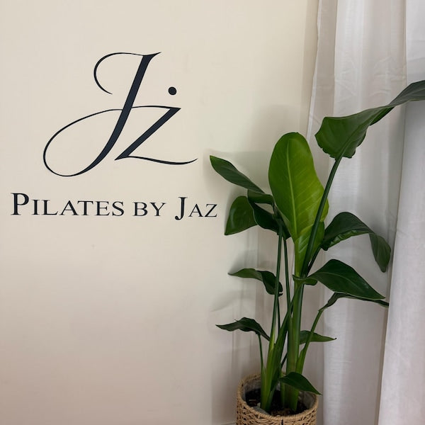Black Pilates by Jaz monogram and lettering on a white wall beside a plant.