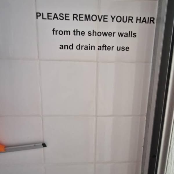 Black custom shower-use instruction lettering on white bathroom tiles.