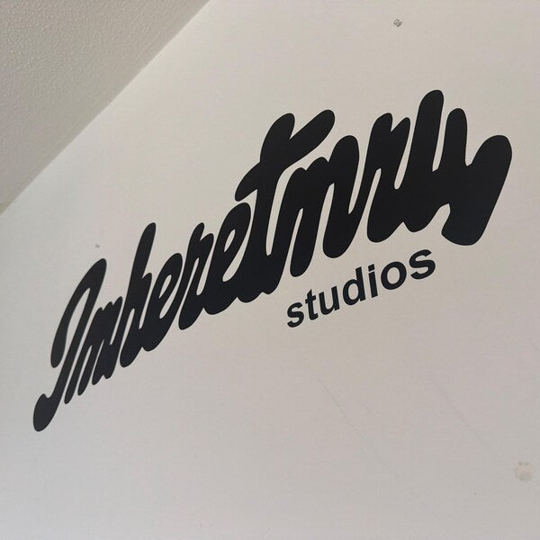 Black script studio logo applied to a white wall.
