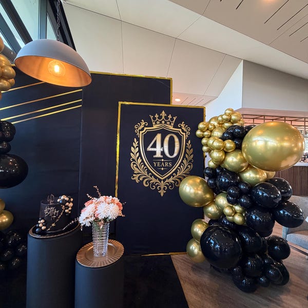Gold 40th birthday crest and lettering on a dark backdrop beside balloons.