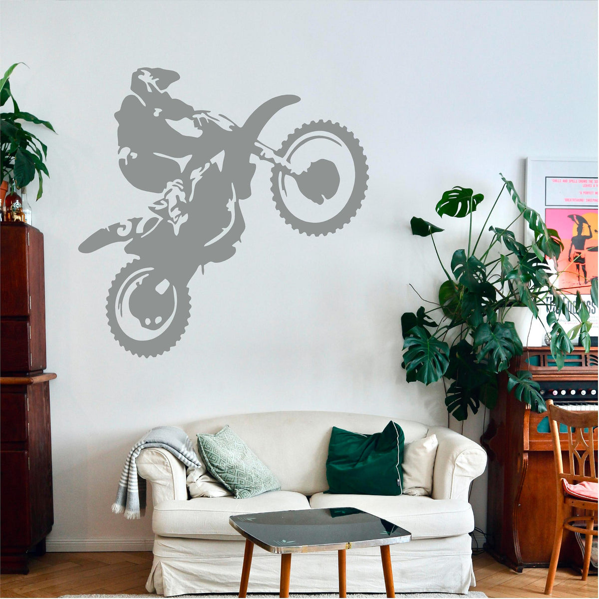 Grey motorbike wheelie rider wall decal above a white loveseat beside plants.
