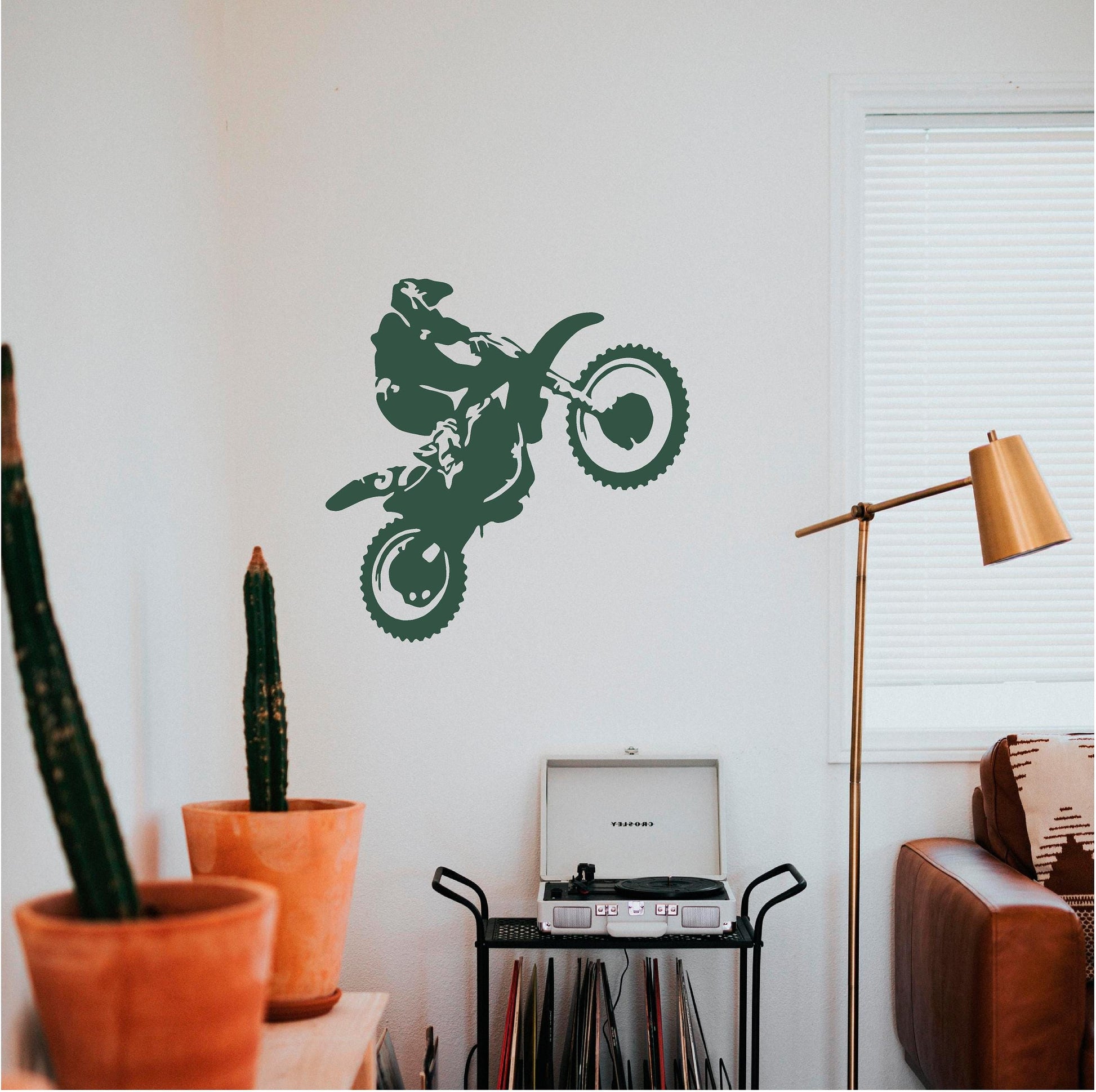 Dark green motorbike wheelie rider wall decal above a record player beside a cactus and copper lamp.
