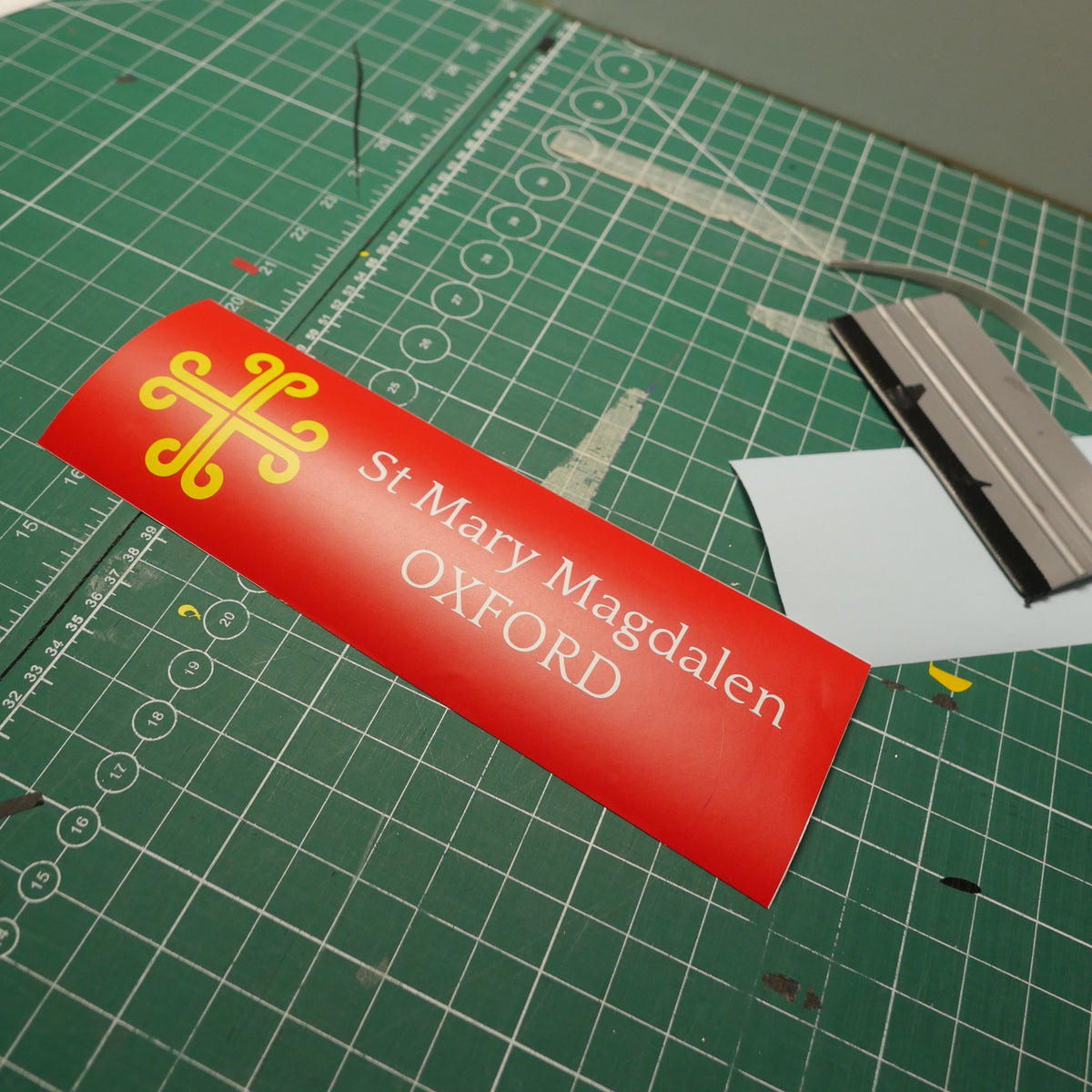 St Mary Magdalen — White lettering and a yellow emblem on a red sign.